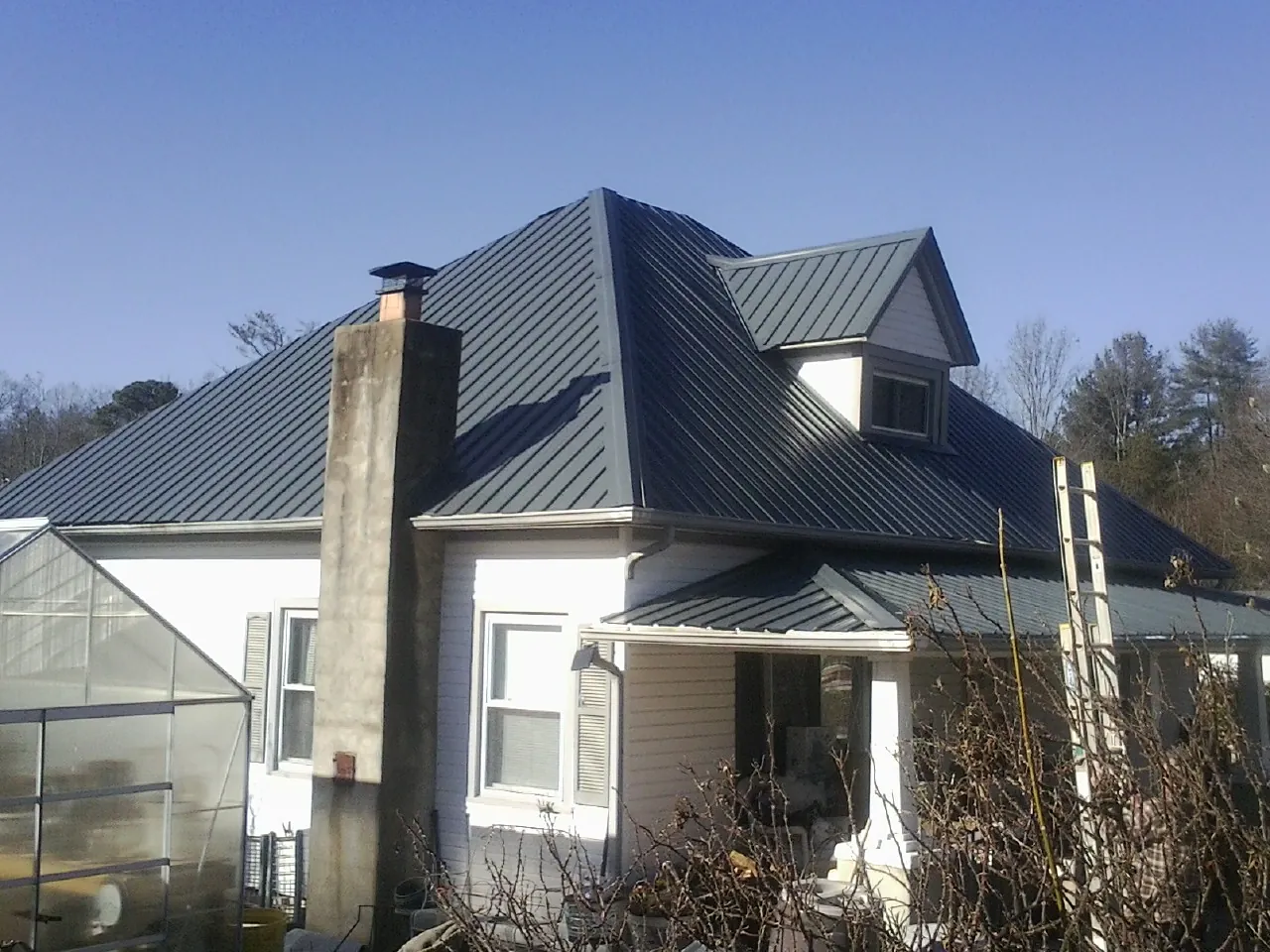 Dark blue standing seam metal roof on a white farmhouse with dormer — Slate & Tile Roof Repair by Roofing Brothers in Taylor