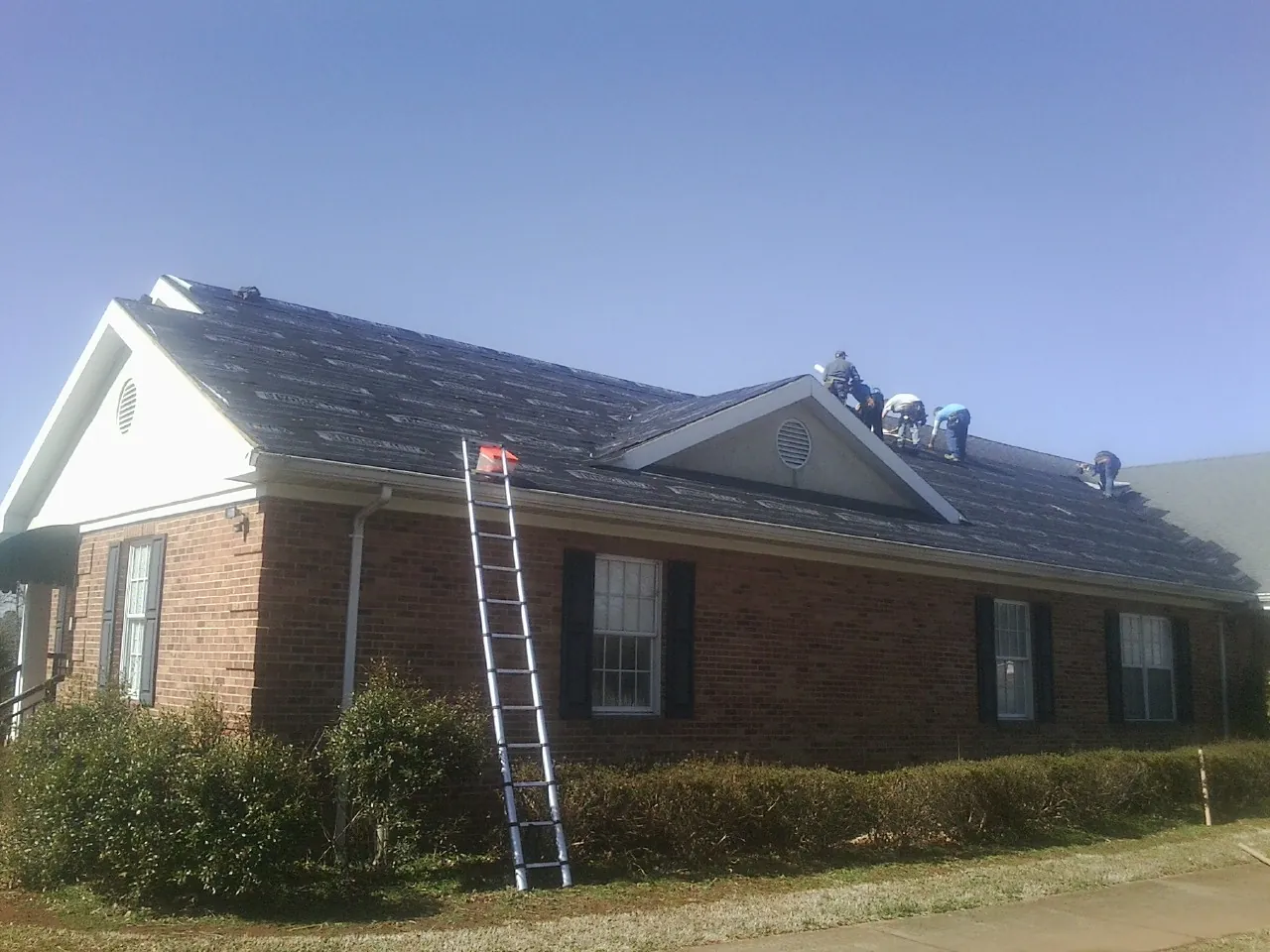Crew tearing shingles off a brick ranch roof with a ladder set — Metal Roof Repair work by our crew in Taylor